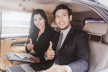 handsome business man and Business woman sitting and Thumbs up in luxury limousine car, working on laptop computer, Works anytime and anywhere concept.