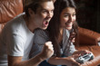 Young female gamer hold joystick, playing video game while spending weekend at home, excited boyfriend cheering her up, supporting her to win race, couple having fun together. Entertainment concept
