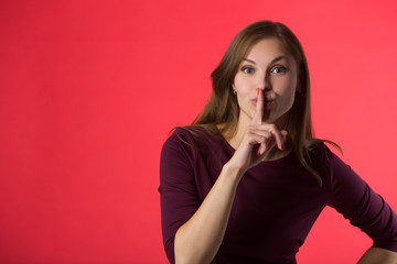 Wall Mural - beautiful young girl with her hair on a red background with a gesture of silence