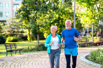 Wall Mural - Happy senior couple jogging outdoors in park.