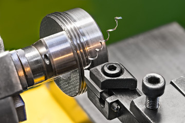 Threading by a steel tool bit on a lathe. Close-up of turning a rotating metallic workpiece clamped in a chuck jaws of the machine tool. Beautiful twisted swarf. Idea of machining and metalwork.