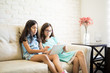 © AntonioDiaz - Hispanic sisters using tablet on the sofa in the living room