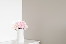 Angle Of White And Gray Walls In Room. On Dresser Stands White Vase With Pink Flowers Blooming Peonies.