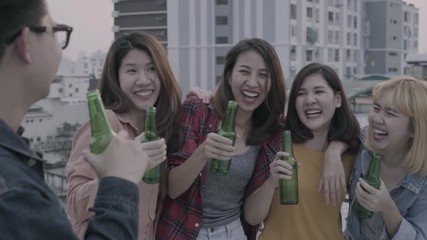 Wall Mural - Slow motion - Group of young asian women and man people dancing and raising their arms up in air music played by dj at sunset urban party on rooftop. Young asian friends hanging out with drinks beer.