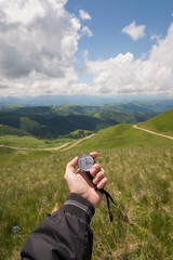 A man's hand of a tourist with an authentic compass on the background of a mountain road landscape