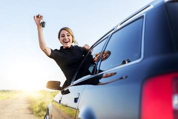 Wall Mural - An attractive woman in a car holds a car key in her hand.