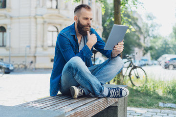 Young man sat on park bench using tablet