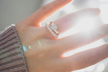 Wall Mural - Close up of elegant diamond ring on woman finger with dark pink sweater winter clothe and sunlight tone. love and wedding concept.soft and selective focus.