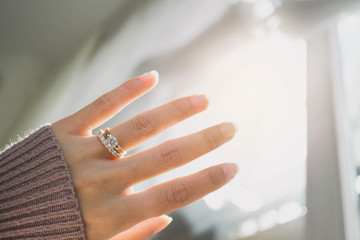 Wall Mural - Close up of elegant diamond ring on woman finger with dark pink sweater winter clothe and sunlight tone. love and wedding concept.soft and selective focus.