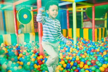 Wall Mural - portrait of cute african-american boy playing in ball pit, having fun in large indoor play center, s