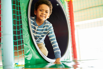 Wall Mural - portrait of cute african-american boy peeking from plastic tunnel while having fun in indoor play ar