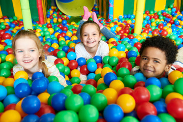 Colorful portrait of three happy kids smiling happily at camera while having fun in ball pit of children play center, copy space