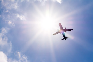 The plane flies in the sky against the sun.
