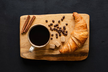 Canvas Print - Coffee and croissant on wooden board over black background, top view