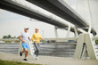© pressmaster - Contemporary senior couple in activewear jogging on bridge along waterside in the morning