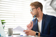 © Yakobchuk Olena - Profile of handsome young male sitting at table and holding papers and blue pencil in hands. He is looking sideways absorbed in personal consideration of business ideas
