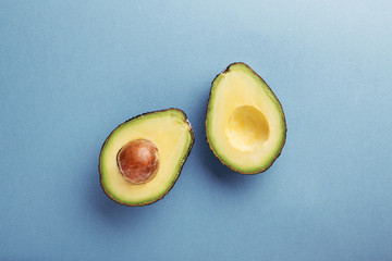 Two halfs of avocado with seed on blue background. Top view, minimal styled composition.