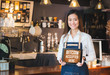 © weedezign - Close up woman barista holding tablet and show bitcoin accepted here on tablet screen at cafe counter bar,seller coffee shop accept payment by crypto currency.digital money concept.modern waitress.
