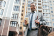 © LIGHTFIELD STUDIOS - bearded smiling businessman in suit with leather bag holding coffee to go