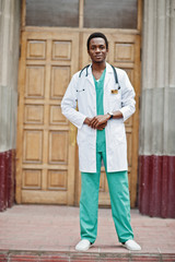 Wall Mural - Stylish african american doctor with stethoscope and lab coat posed against door of hospital.