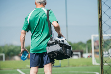 back view of old man with sportive water bottle and bag on soccer field