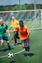 multiracial old men playing football together on green field