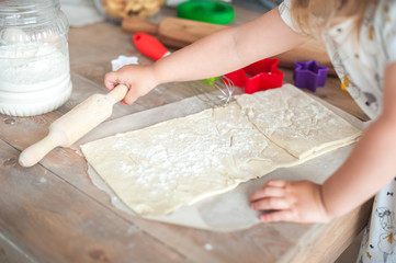 The process of baking from dough. Baby hands roll out the dough and make cookies in the form of asterisks on the dough