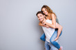 © deagreez - Portrait with copysapce of attractive lovely couple, strong man carrying on back charming woman with curly hair looking at camera isolated on grey background