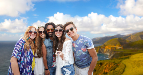 Sticker - tourism, travel and summer holidays concept - smiling young hippie friends taking picture by selfie stick over big sur coast of california background