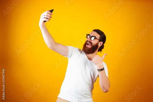 Fotografía Young Cheerful man taking a selfie on his smartphone wearing a white T-shirt and earpods
