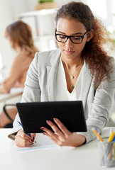 business, technology and people concept - african american businesswoman with tablet pc computer filling papers at office