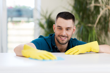 Wall Mural - household, cleaning and people concept - smiling man wiping table with cloth at home