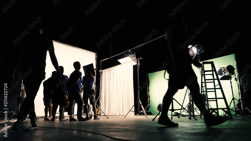 Behind the scenes of TV commercial movie film or video shooting production which crew team and camera man setting up green screen for chroma key technique in big studio.