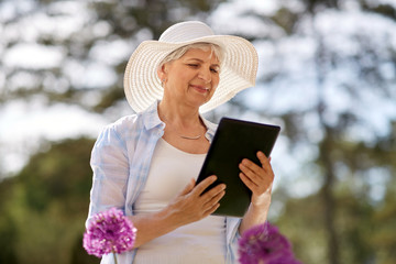 Canvas Print - gardening, technology and people concept - happy senior woman with tablet pc computer and flowers at summer garden