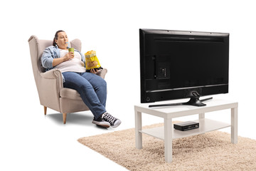 Overweight woman with a bag of chips and a drink sitting in an armchair and watching television