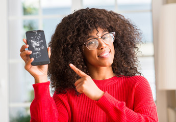 Poster - African american woman holding broken smartphone very happy pointing with hand and finger to the side