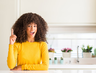 Sticker - African american woman wearing yellow sweater at kitchen pointing finger up with successful idea. Exited and happy. Number one.