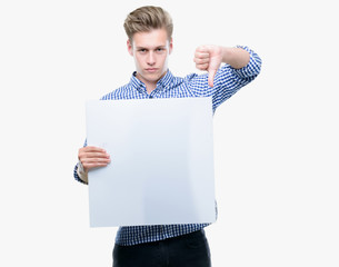 Poster - Young handsome blond man holding a banner with angry face, negative sign showing dislike with thumbs down, rejection concept