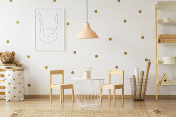 Wall Mural - Pastel lamp above table between chairs in gold kid's room interior with poster. Real photo