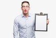 © Krakenimages.com - Handsome young business man showing a clipboard scared in shock with a surprise face, afraid and excited with fear expression