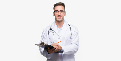 Sticker - Handsome young doctor man holding a clipboard with a happy face standing and smiling with a confident smile showing teeth