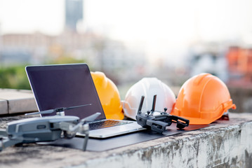 Wall Mural - Drone, laptop computer and protective helmet at construction site. Using unmanned aerial vehicle (UAV) for land and building site survey in civil engineering project.