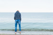 © Konstiantyn Zap - A woman dressed in jeans and a sweater stands on the seashore in the water. Concept Women's loneliness, depression.