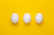 Three white eggs on a yellow background. Top view