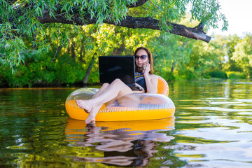 Wall Mural - Woman freelancer working on a laptop sitting in an inflatable ring, remote work.