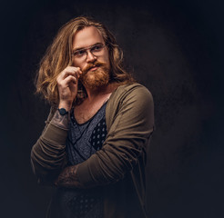 Wall Mural - Portrait of tattoed redhead hipster male with long luxuriant hair and full beard dressed in a t-shirt and jacket holds a keeps the scarecrow of an owl and fox skin on a shoulder in a studio.