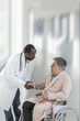 © JPC-PROD - African ,American,male doctor greeting recovering senior patient in wheelchair in hospital handshake