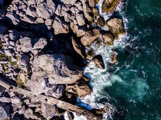 Poster - aerial overhead view of waves crash into the stone rocky sea coast