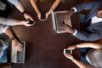 Top view of diverse gadget addicts using devices, not talking during friendly meeting, multiracial people lost in virtual reality, being obsessed with technology, busy with laptops and smartphones