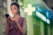 a young asian woman is locating a pharmacy store at night with her smart phone mobile device. Communicate about open pharmacies during night time, using navigation to locate them, health, on call